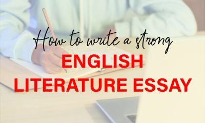 A focused student writing an English literature essay with open books and a laptop on a wooden desk.